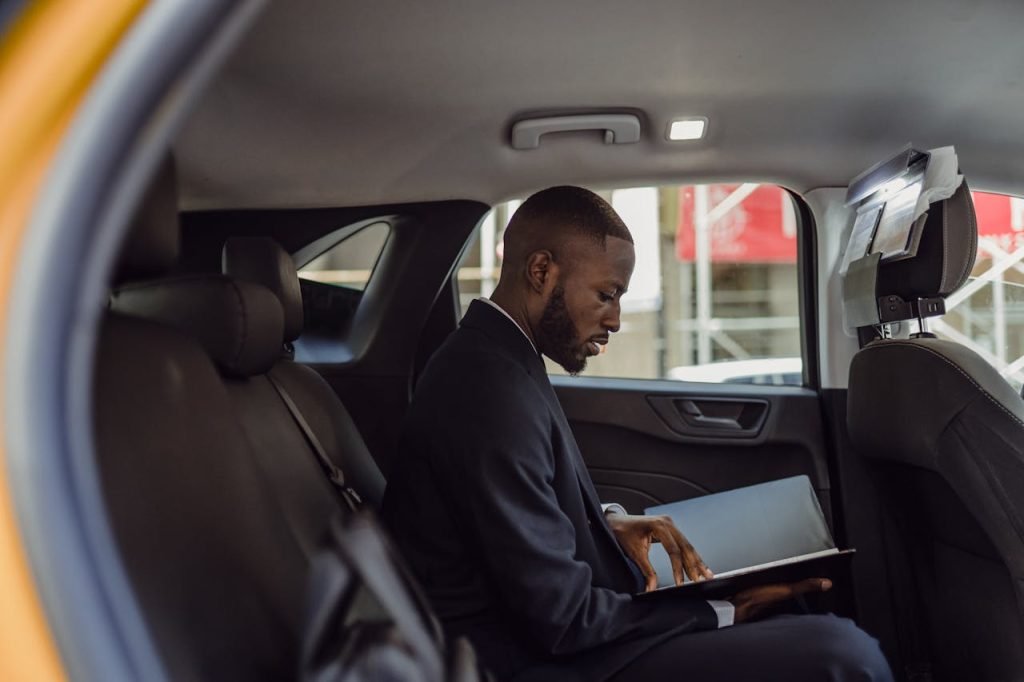 A professional man in a suit reads documents while sitting in a car interior, conveying a business theme.